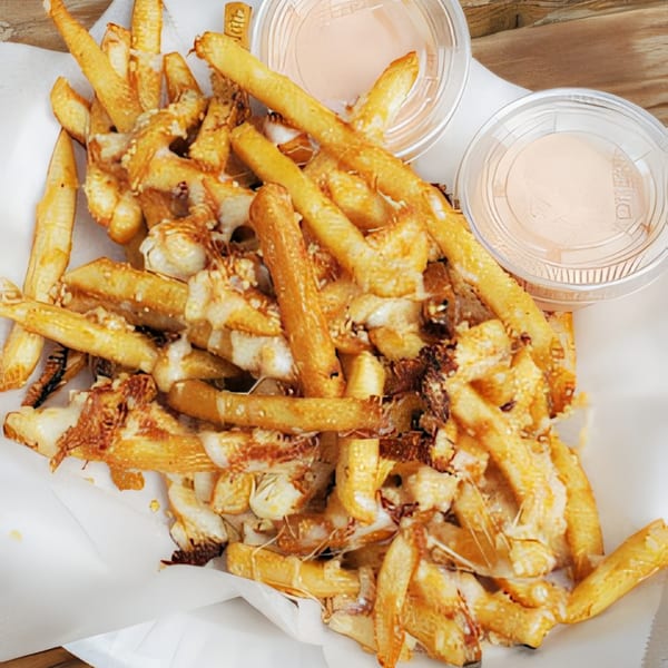 A basket of golden french fries topped with melted cheese and two dipping sauces.