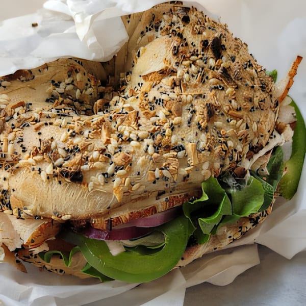 A Wasatch Bagel and Grill everything bagel sandwich with lettuce, red onion, and green pepper.