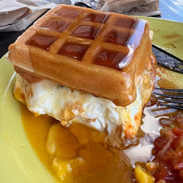 A waffle sandwich with a fried egg and bacon, drizzled with syrup, on a lime green plate.