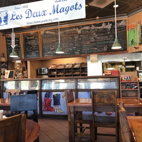 Interior view of Wasatch Bagel and Grill, showing the counter, menu boards, and wooden tables and chairs.