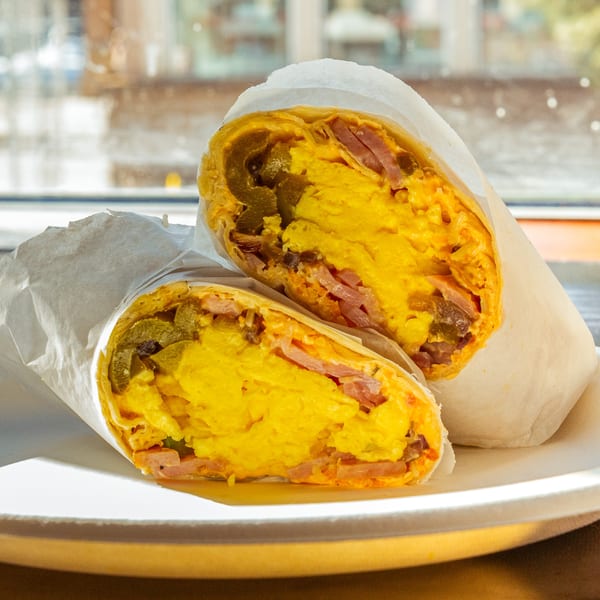 Two halves of a breakfast burrito with scrambled eggs, ham, and jalapeños on a white plate.