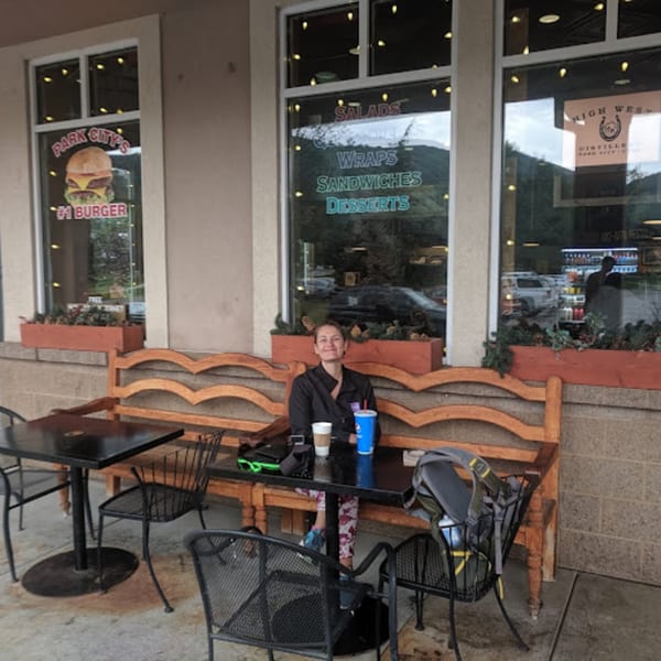 A woman sits at an outdoor table with drinks in front of Wasatch Bagel and Grill.