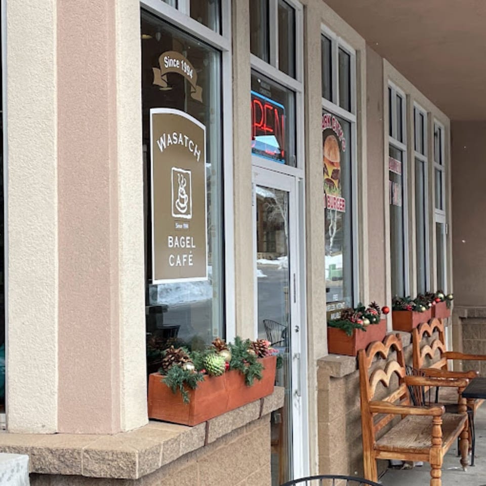 Exterior of Wasatch Bagel Cafe with a brown sign, window boxes, and outdoor seating.